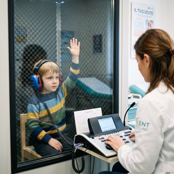 Bambino di circa 6 anni esegue un esame audiometrico in cabina silente con cuffie audiometriche, alzando la mano alla percezione del suono